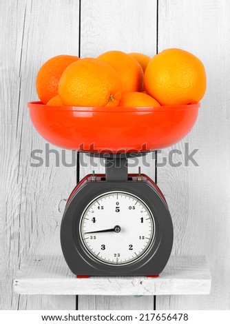Oranges on scales on a wooden shelf.