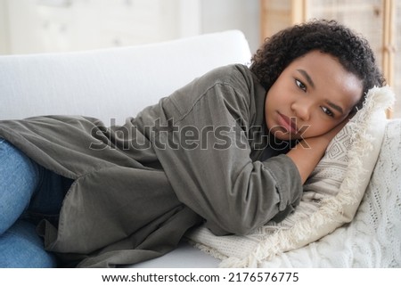 Frustrated lonely teen girl is lying on couch at home. Depressed african american teenager is suffering bullying or violence. Hispanic girl is desperate. Anxiety, stress and health problem concept. Royalty-Free Stock Photo #2176576775