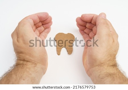 On a white background, the symbol of the tooth inside the hands of a man. Healthy teeth concept