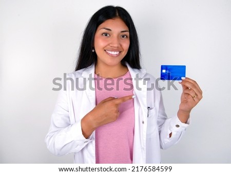Photo portrait of Young hispanic doctor girl wearing coat over white background doing purchase with pointing finger credit bank card