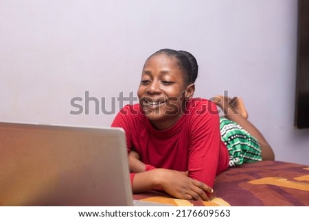 A young black teenage girl smiling looking laptop whilst lying on bed Royalty-Free Stock Photo #2176609563