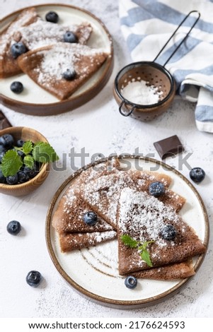 Celebrating Pancake day, healthy breakfast. Delicious homemade chocolate crepes with blueberries on a stone countertop. 