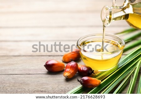 Pouring palm oil into glass bowl with fresh palm nuts on wooden table. Royalty-Free Stock Photo #2176628693