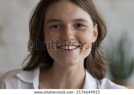 Close up sun spotted face without make up of attractive young freckled woman, cropped image. Caucasian female posing alone indoor smile look at camera. Natural beauty, young generation person concept