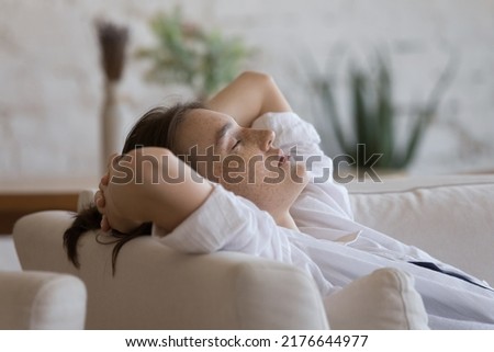Close up woman falls asleep on sofa with hands behind head, relieve fatigue, relax on cozy soft furniture at home. Accommodation in hotel, free time, fresh conditioned air inside, comfort life concept Royalty-Free Stock Photo #2176644977
