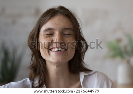 Close up shot happy freckled woman laughing with eyes closed. Head shot portrait cheerful girl having wide toothy smile looks overjoyed. Skincare products for young skin covered with sunspots concept Royalty-Free Stock Photo #2176644979