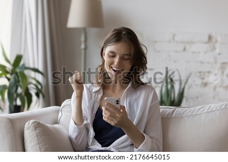 Freckled woman sit on couch holds smartphone read great news in sms feels overjoyed, celebrate university admission notice, fantastic commercial offer get, sell-out of favourite fashion store concept Royalty-Free Stock Photo #2176645015
