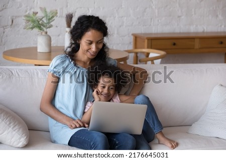 African mom and daughter enjoy movies on laptop relax on sofa looks at screen watch on-line cartoons, amusing content in video vlog, spend leisure at home. Children development use modern tech concept