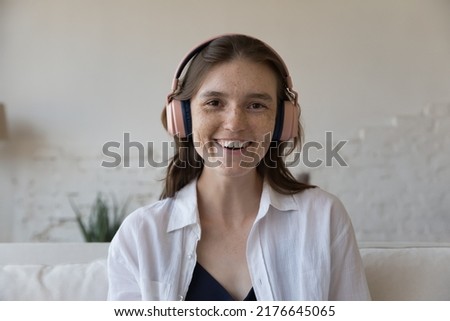 Head shot portrait attractive freckled woman in headphones staring at camera, make distance conversation via video conference app call at home. Seeker pass job interview, streaming event, tech concept Royalty-Free Stock Photo #2176645065