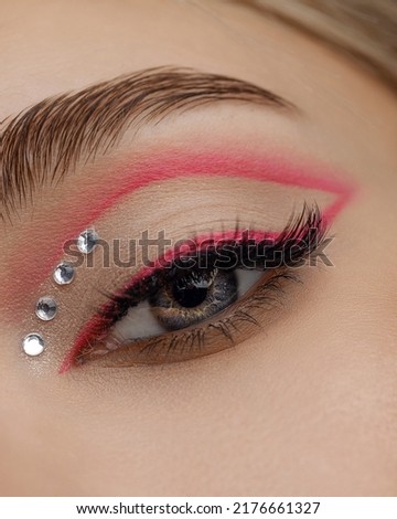 Creative pink eye makeup with arrow and rhinestones. Beautiful macro shot of female eye make-up. Blue eye. Creative make-up. Perfect shape make-up and long lashes. Cosmetics. Close-up Royalty-Free Stock Photo #2176661327