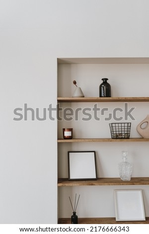 Aesthetic modern minimalist Scandinavian home interior decorations. Elegant bohemian living room with white wall, shelves with candle, picture frame, storage box, bottle, vase, fragrance