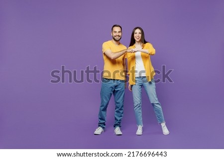 Full body young smiling happy couple two friends family man woman together in yellow casual clothes looking camera giving a fist bump in agreement isolated on plain violet background studio portrait Royalty-Free Stock Photo #2176696443