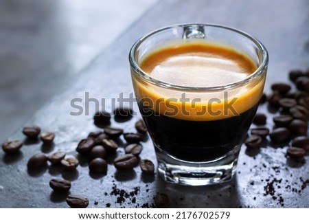 Closeup cup of hot espresso with a nice crema on a rustic concrete table with a pile of roasted arabica coffee beans. Royalty-Free Stock Photo #2176702579