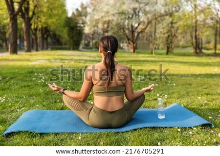 Back view of peaceful young black woman meditating in lotus pose, doing morning yoga practice, sitting on sports mat outdoors, copy space. Active lifestyle, mindfulness concept