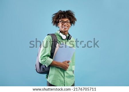 Smart african american student guy with backpack and notebooks smiling at camera, posing over blue studio background. Education, university, college, studying, course concept Royalty-Free Stock Photo #2176705711