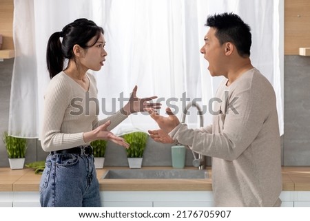 Relationship problems concept. Angry asian woman arguing with her husband at kitchen, mad spouses shouting at each other and gesturing, having difficulties in marriage, side view, copy space Royalty-Free Stock Photo #2176705907