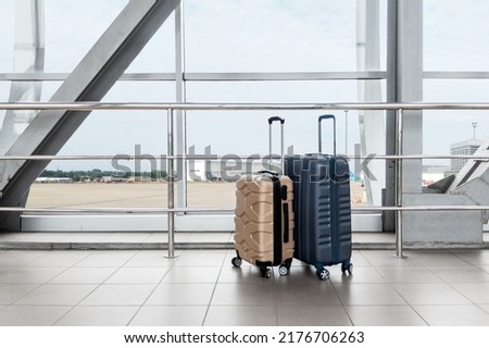 Two Stylish Plastic Luggage Suitcases Standing Near Panoramic Window At Airport, Blue And Beige Travel Bags Waiting In Terminal, Creative Shot For Transportration And Travelling Concept, Copy Space Royalty-Free Stock Photo #2176706263
