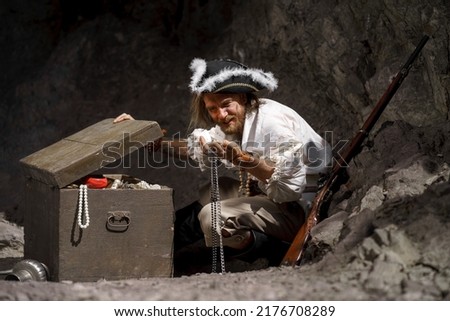 Sea robber captain of pirate ship armed with treasure chest in cave. Concept historical halloween. Filibuster cosplay.