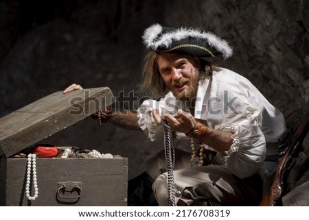 Sea robber captain of pirate ship armed with treasure chest in cave. Concept historical halloween. Filibuster cosplay. Royalty-Free Stock Photo #2176708319