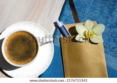 A cup of coffee on a white table. Nearby are an envelope with a pen, an Orchid flower and a turquoise scarf. Date invitation.