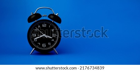 Black alarm clock on blue background, importance of time concept and time work.