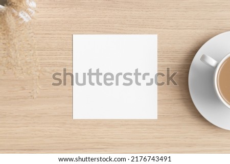 Square invitation card mockup with a dry flower on the wooden table.
