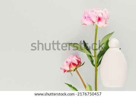 Mock up of natural, flower beauty product. White cosmetic bottle with two beautiful, pink peonies on a blue background with copy space. Minimalist composition with flowers and cosmetic product