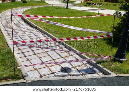 Warning or cordon tape to stop pedestrians. Red and white lines of barrier row tape prohibit passage. Dismantling of old pavement of pedestrian path in park. Renovation, Garden architecture