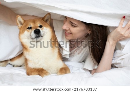 Funny girl woman playing with her shiba inu set dog in bed in a hotel. Family time friends