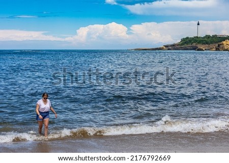 Young girl coming out of the sea on the beach of Biarritz with the lighthouse in the background.