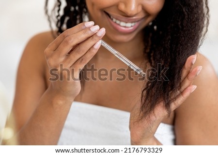 Split Ends Care. Smiling African American Woman Applying Moisturising Oil To Her Curly Hair, Closeup Of Young Black Female Putting Haircare Product With Dropper While Making Beauty Routine At Home Royalty-Free Stock Photo #2176793329