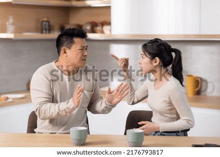 Relationship problems concept. Angry asian woman arguing with husband while drinking coffee at kitchen, mad spouses shouting at each other and gesturing, having difficulties in marriage, copy space Royalty-Free Stock Photo #2176793817
