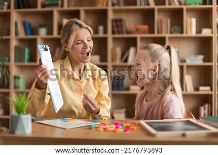 Cheerful female speech therapist curing child's problems and impediments, little girl learning letters with private English language tutor during lesson Royalty-Free Stock Photo #2176793893