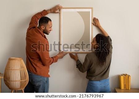 Black Husband And Wife Hanging Picture In Frame On Wall At Home. Married Couple Decorating Room With Poster Together. Interior Design, Art And Decoration Concept Royalty-Free Stock Photo #2176793967