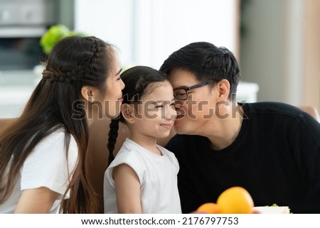 Asian father and mother Show your love to little daughter and having breakfast together happily in the dining room of the house.