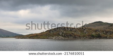 Panoramic view of the rocky shores of Kyles of Bute from the water. Hills and mountains in the background. Dark storm sky. Bute island, Firth of Clyde, Scotland, UK
