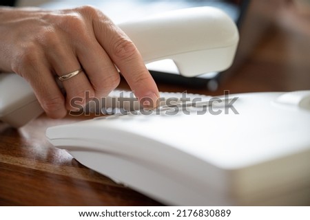 Closeup view of female hand dialing telephone number using white landline phone. Royalty-Free Stock Photo #2176830889