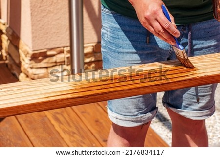 Close up male hands holding a brush and painting a rough varnish on the background of the surface of a wooden board Royalty-Free Stock Photo #2176834117