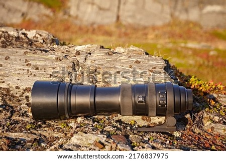 Tele lens from camera on the background of grass and stones in the tundra. Modern photographic equipment in the bright sunset light at the outdoor