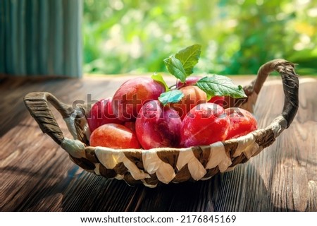 wicker basket filled with red plums on a rustic table. photographed in natural light in real life