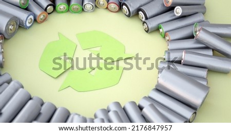 Used AA batteries and proper disposal of environmentally and soil-toxic batteries on a green background. The concept of processing harmful and recyclable objects.