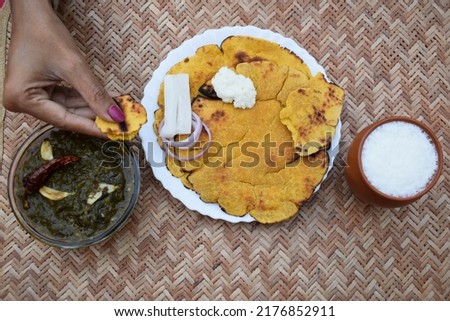 Person eating on table Indian popular dish makki di roti and Sarson da saag, mustard leaves curry and unleavened maize flour bread served in an authentic way with white butter and green chilly. Royalty-Free Stock Photo #2176852911