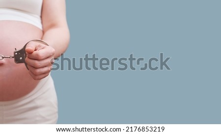 Chained hands of a pregnant woman, studio shot on a blue background, copy space with a place under the text on the prohibition of abortions