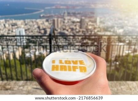 The caption I LOVE HAIFA in a cup of coffee and a view of Haifa city in the background.