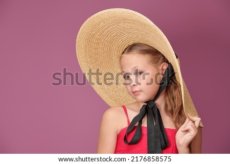 A lovely girl with wavy blonde hair poses in a summer wide-brimmed hat and pink dress. Purple background. Kid's summer fashion. Summer style. Little lady. Copy space.
