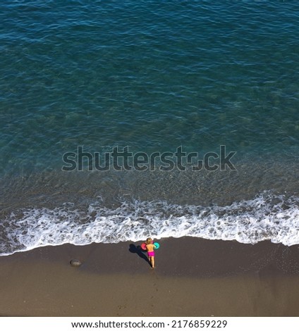 Top view of one little blonde child playing on the seashore with waves
