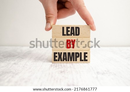 On a light background, wooden cubes and a wooden block with the text lead by example