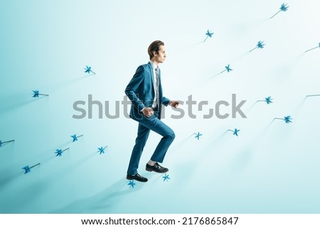 Attractive businessman in suit walking on abstract wall with many dart arrows. Goal setting and strategy concept