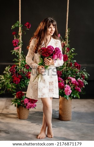 a beautiful young woman in a white dress near the swing in peony flowers. femininity and beauty. perfumes and cosmetics for women. happiness. flower therapy. decor for celebration and photo shoot.