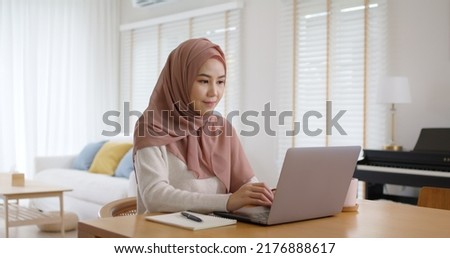 Young Gen Z workforce islam woman self learn MBA online class reskill upskill job at home. Asia people arab girl study relax sit at table wear hijab scarf write or typing e-mail work on digital laptop